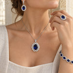 Sapphire-blue jewelry set worn: pendant necklace, drop earring, ring and bracelet
