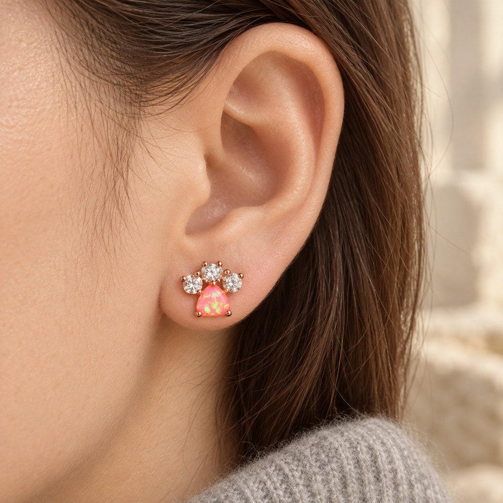 Dog paw stud earring with a pink fire opal pad, worn on a woman's ear