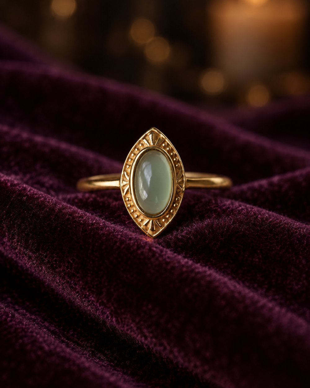 Sage-green cabochon ring with an engraved gold-tone frame, standing in velvet
