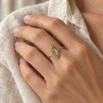 Sage-green marquise ring in gold-tone, worn on a woman's finger