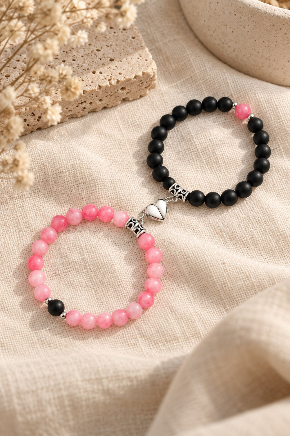 Matching magnetic heart bracelets clicked together on cream linen