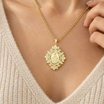 Ornate gold-tone Miraculous Medal pendant worn with a cream knit top