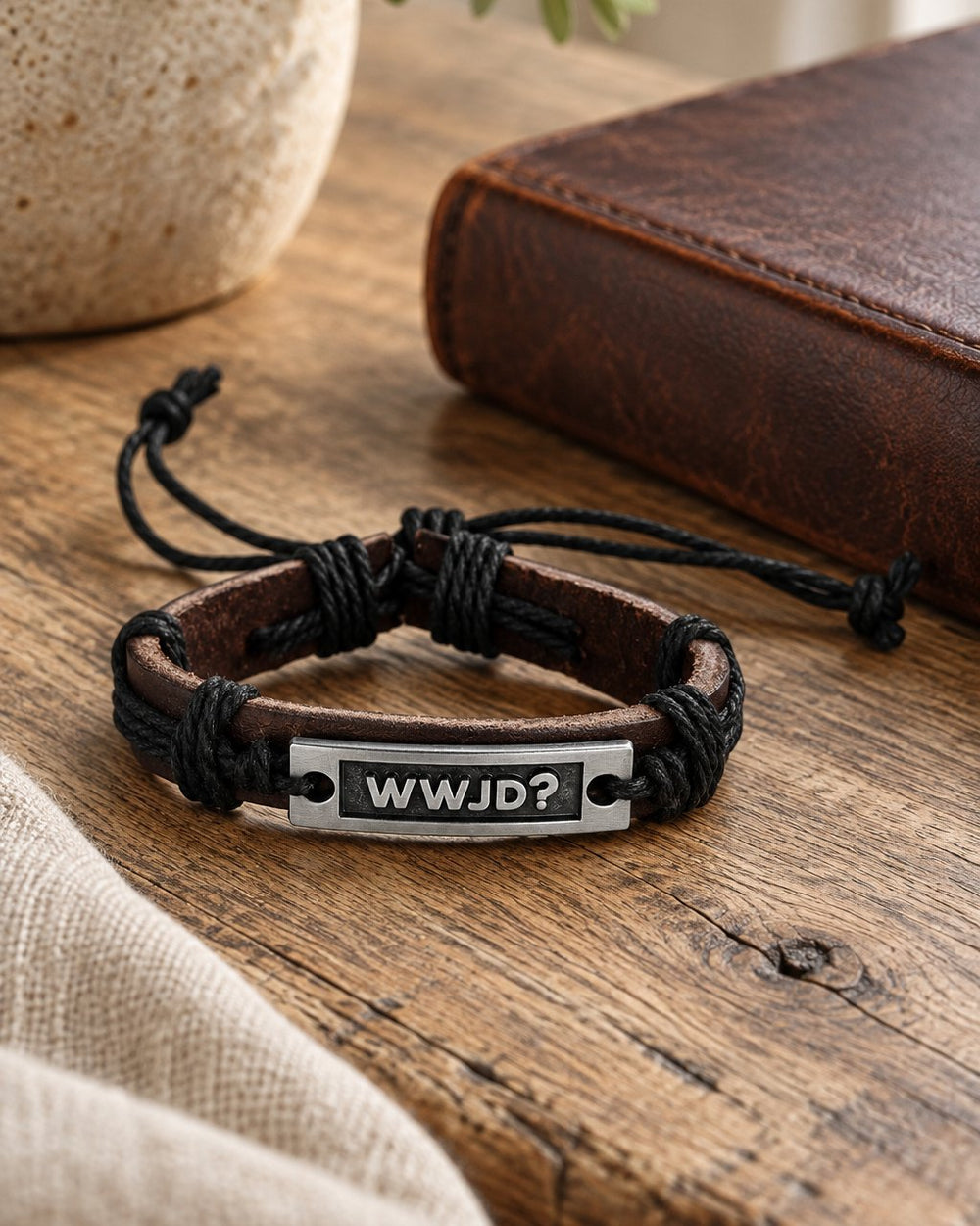 WWJD leather cuff bracelet on an oak table beside a leather-bound book